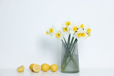 Photo of Beautiful daffodils in vase and lemons on white table indoors