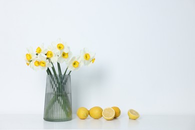 Photo of Beautiful daffodils in vase and lemons on white table indoors
