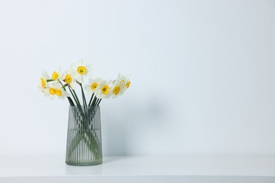 Photo of Beautiful daffodils in vase on white table indoors, space for text