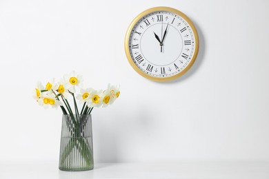 Photo of Beautiful daffodils in vase on white table and clock indoors
