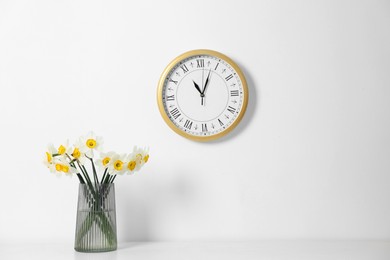 Photo of Beautiful daffodils in vase on white table and clock indoors