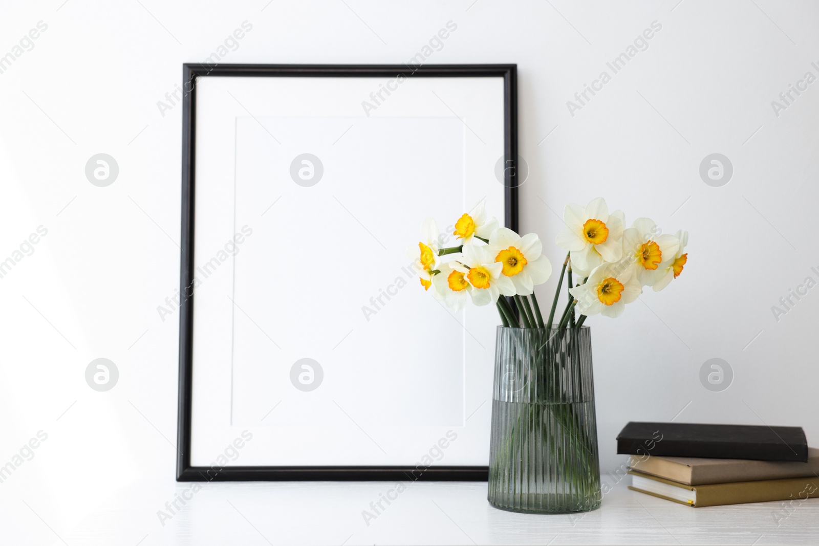 Beautiful daffodils in vase, picture frame and books on white table indoors Photo of Beautiful daffodils in vase, picture frame and books on white table indoors