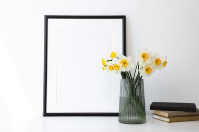 Photo of Beautiful daffodils in vase, picture frame and books on white table indoors