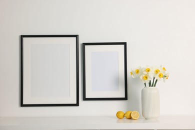 Photo of Beautiful daffodils in vase on white table and picture frames indoors