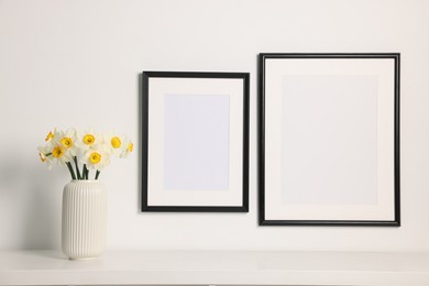 Photo of Beautiful daffodils in vase on white table and picture frames indoors
