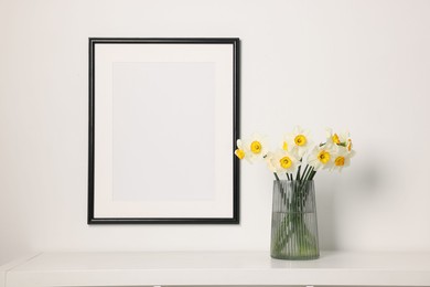 Photo of Beautiful daffodils in vase on white table and picture frame indoors