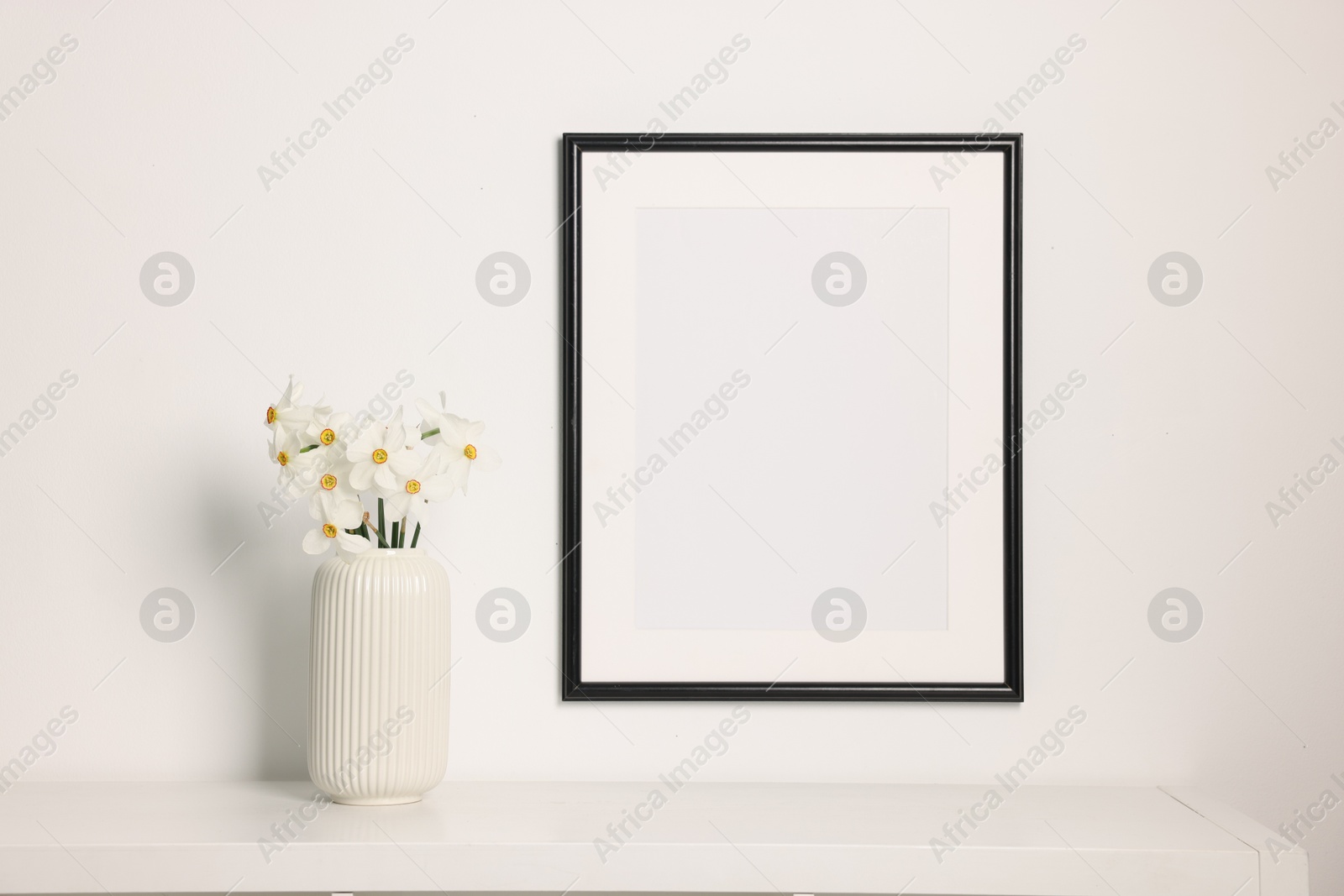 Beautiful daffodils in vase on white table and picture frame indoors Photo of Beautiful daffodils in vase on white table and picture frame indoors