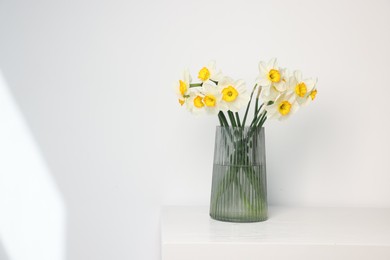 Photo of Beautiful daffodils in vase on white wooden table indoors, space for text