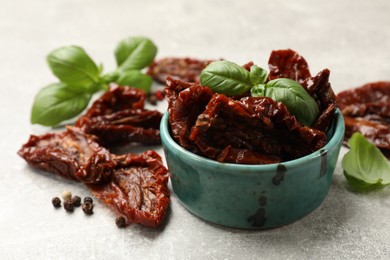 Photo of Delicious sun dried tomatoes in bowl and spices on gray textured table, closeup