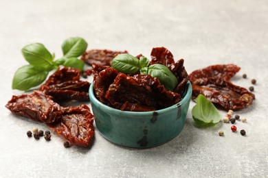 Photo of Delicious sun dried tomatoes in bowl and spices on gray textured table, closeup