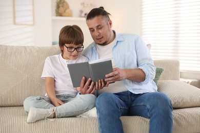 Photo of Father and his son reading book together on sofa at home