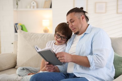 Photo of Father and his son reading book together on sofa at home