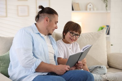 Photo of Father and his son reading book together on sofa at home