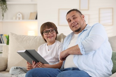 Photo of Father and his son reading book together on sofa at home