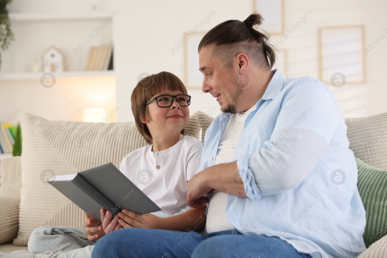 Father and his son reading book together on sofa at home Photo of Father and his son reading book together on sofa at home