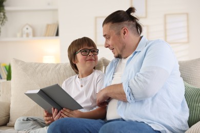 Photo of Father and his son reading book together on sofa at home
