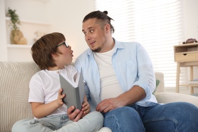 Photo of Father and his son reading book together on sofa at home