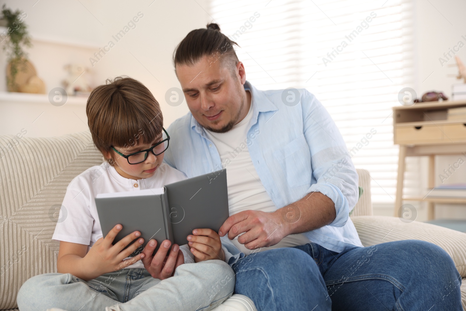 Father and his son reading book together on sofa at home Photo of Father and his son reading book together on sofa at home