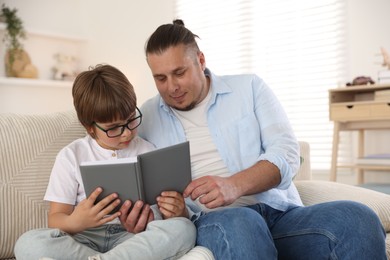 Photo of Father and his son reading book together on sofa at home