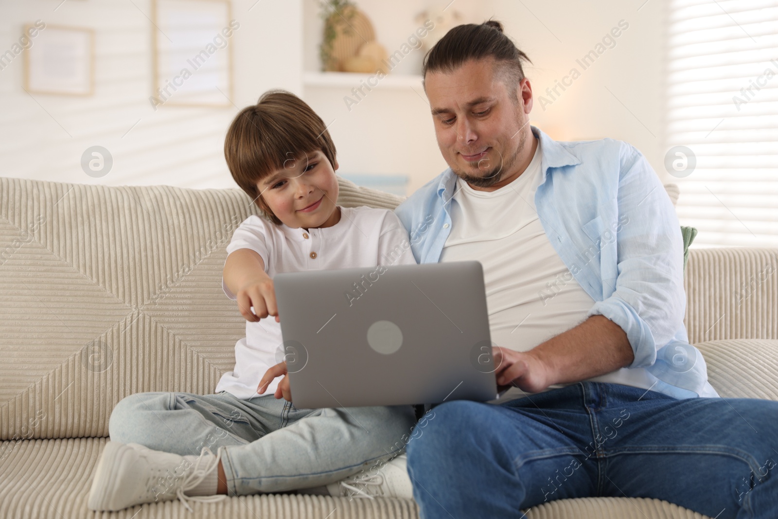 Father and his son watching something on laptop at home Photo of Father and his son watching something on laptop at home