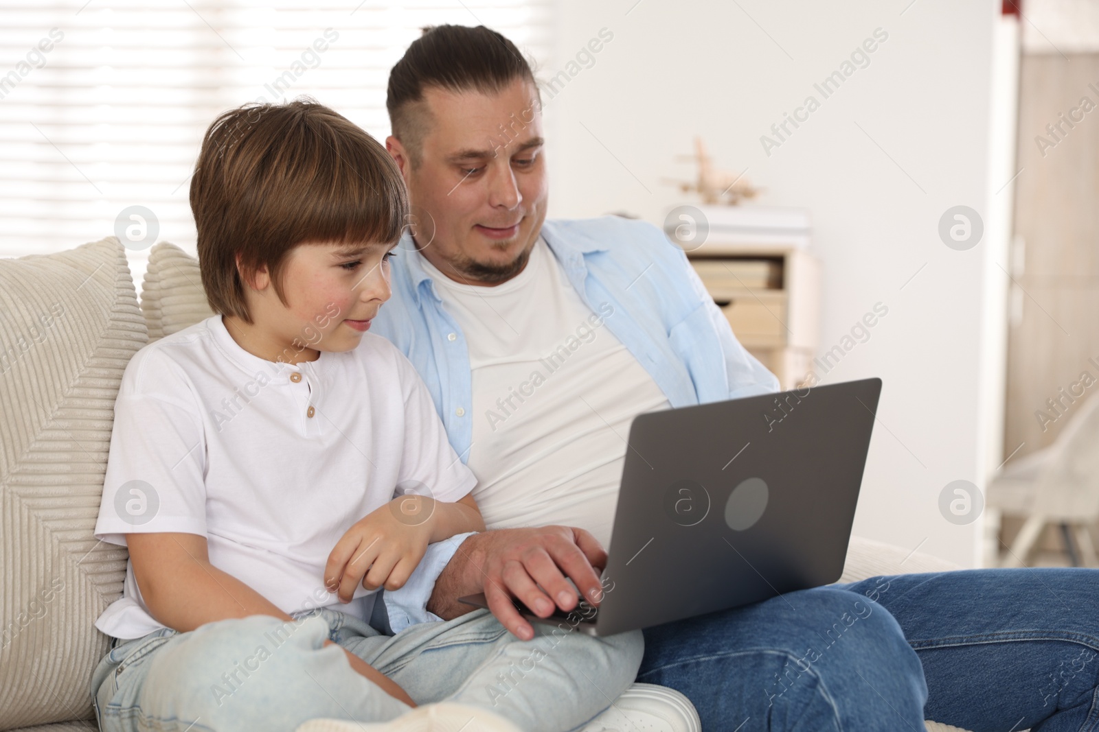 Father and his son watching something on laptop at home Photo of Father and his son watching something on laptop at home