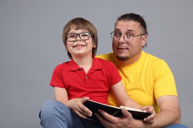 Photo of Father and his son reading book together on grey background