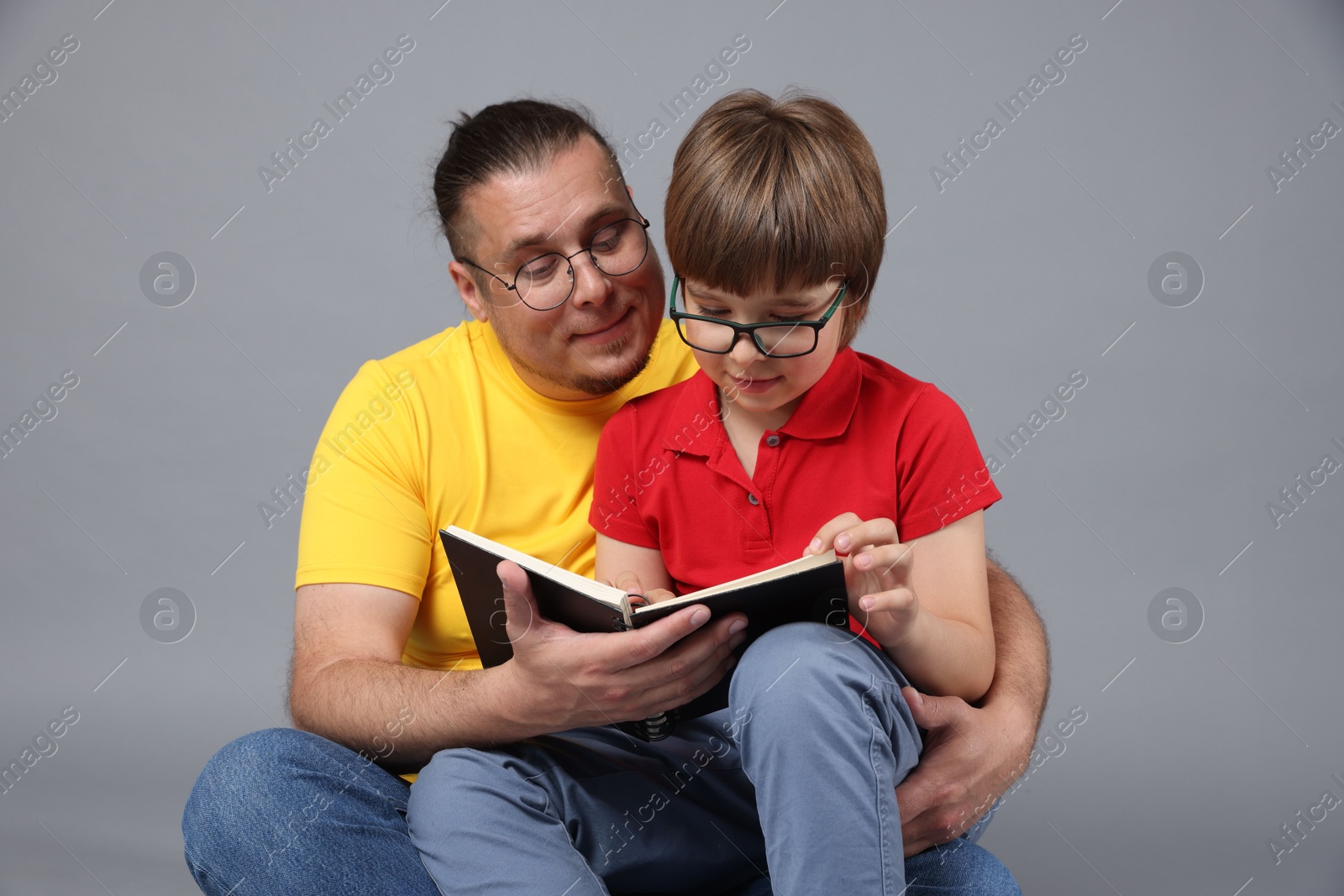 Father and his son reading book together on grey background Photo of Father and his son reading book together on grey background