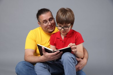 Photo of Father and his son reading book together on grey background