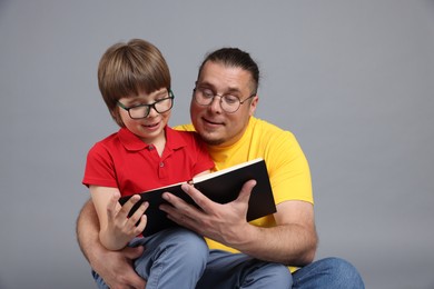 Photo of Father and his son reading book together on grey background