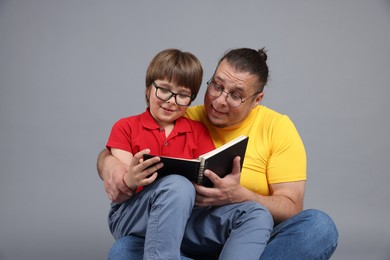 Photo of Father and his son reading book together on grey background