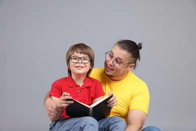 Photo of Father and his son reading book together on grey background
