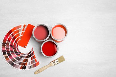 Image of Cans with paint in shades of red, brush and color palette on white background, top view. Space for text