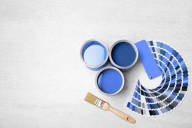 Image of Cans with paint in shades of blue, brush and color palette on white background, top view. Space for text