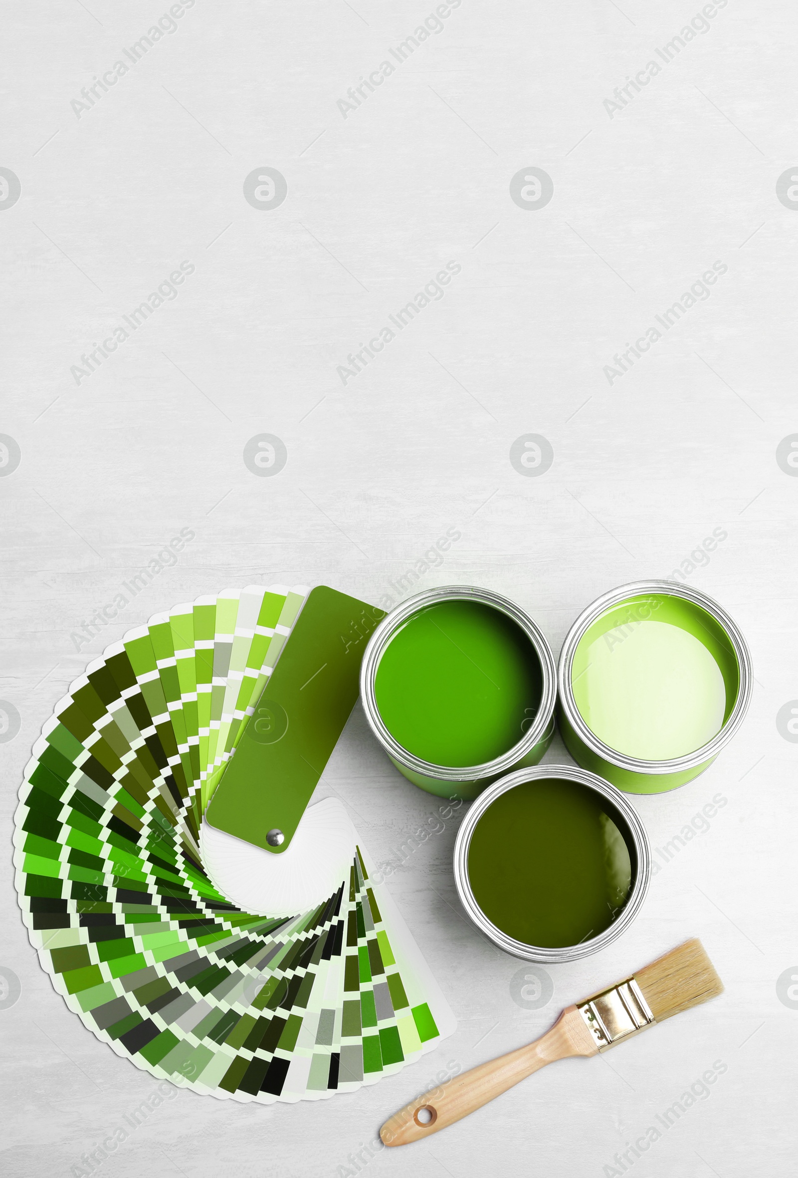 Cans with paint in shades of green, brush and color palette on white background, top view. Space for text Image of Cans with paint in shades of green, brush and color palette on white background, top view. Space for text