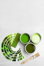 Image of Cans with paint in shades of green, brush and color palette on white background, top view. Space for text