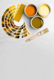 Image of Cans with paint in shades of yellow, brush and color palette on white background, top view. Space for text