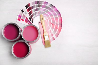 Image of Cans with paint in shades of pink, brush and color palette on white background, top view. Space for text