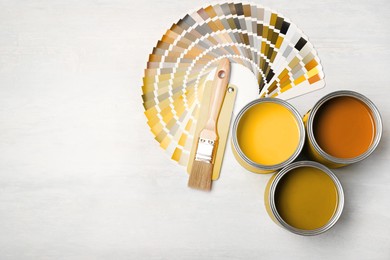 Image of Cans with paint in shades of yellow, brush and color palette on white background, top view. Space for text
