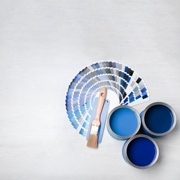 Image of Cans with paint in shades of blue, brush and color palette on white background, top view