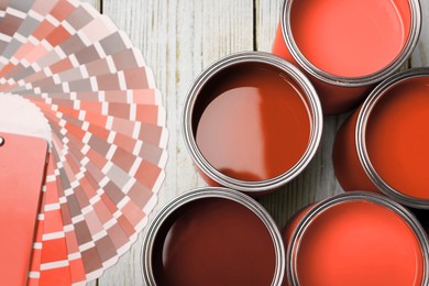 Image of Cans with paint in shades of red and color palette on white wooden background, top view