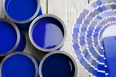 Image of Cans with paint in shades of blue and color palette on white wooden background, top view