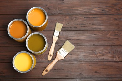 Image of Cans with paint in shades of yellow and brushes on wooden background, top view. Space for text