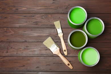Image of Cans with paint in shades of green and brushes on wooden background, top view. Space for text