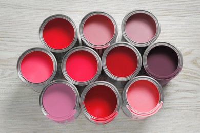 Image of Cans with paint in shades of red and pink on white wooden background, top view