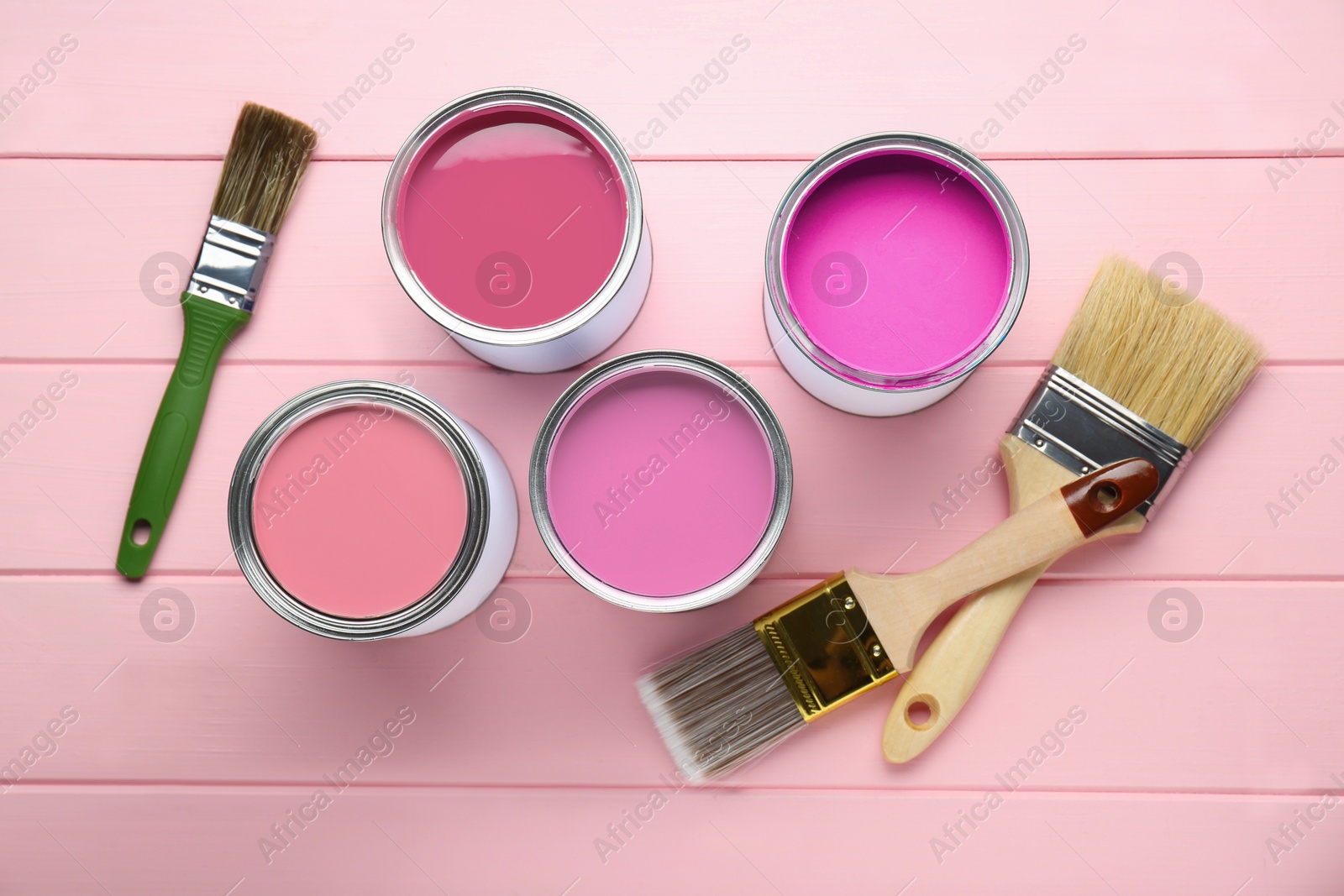 Cans with paint in shades of pink and brushes on color wooden background, top view Image of Cans with paint in shades of pink and brushes on color wooden background, top view