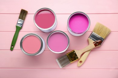 Image of Cans with paint in shades of pink and brushes on color wooden background, top view