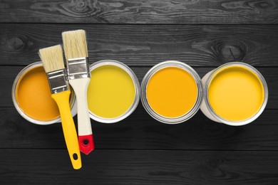 Image of Cans with paint in shades of yellow and brushes on black wooden background, top view