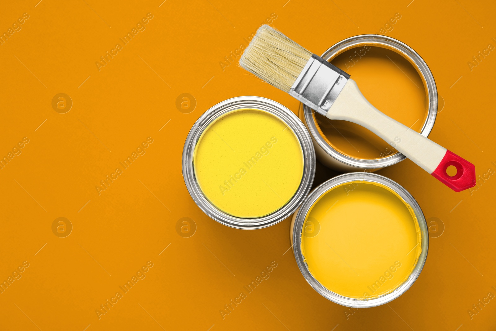 Cans with paint in shades of yellow and brush on orange background, top view. Space for text Image of Cans with paint in shades of yellow and brush on orange background, top view. Space for text