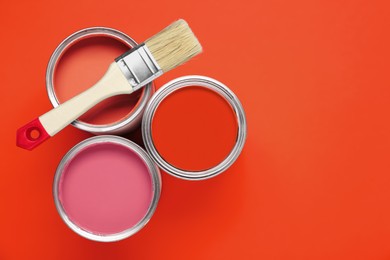 Image of Cans with paint in shades of red and brush on color background, top view. Space for text