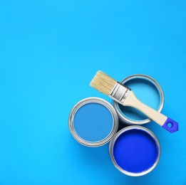 Image of Cans with paint in shades of blue and brush on color background, top view. Space for text